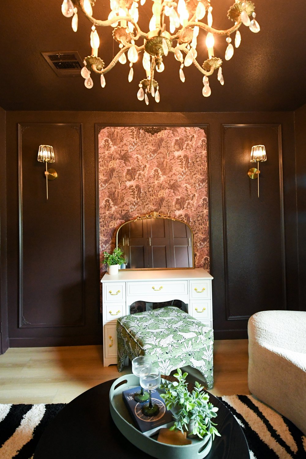 Dressing room end wall with an antique vanity in a wallpapered arched niche and a chandelier