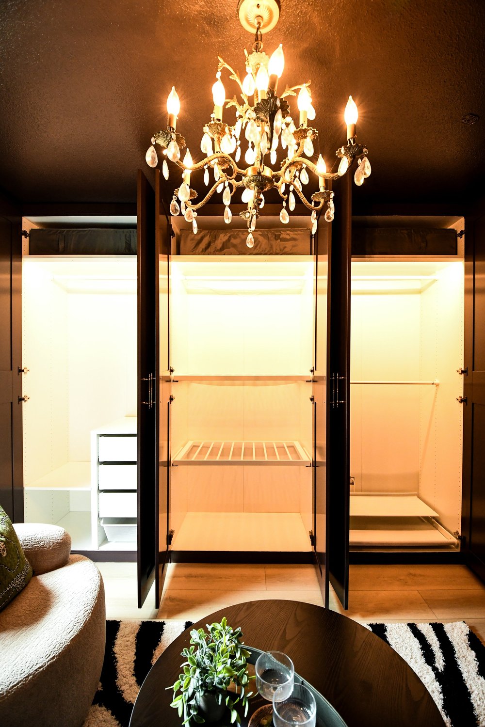 Glass front wardrobe cabinets lit from within beneath the brass chandelier