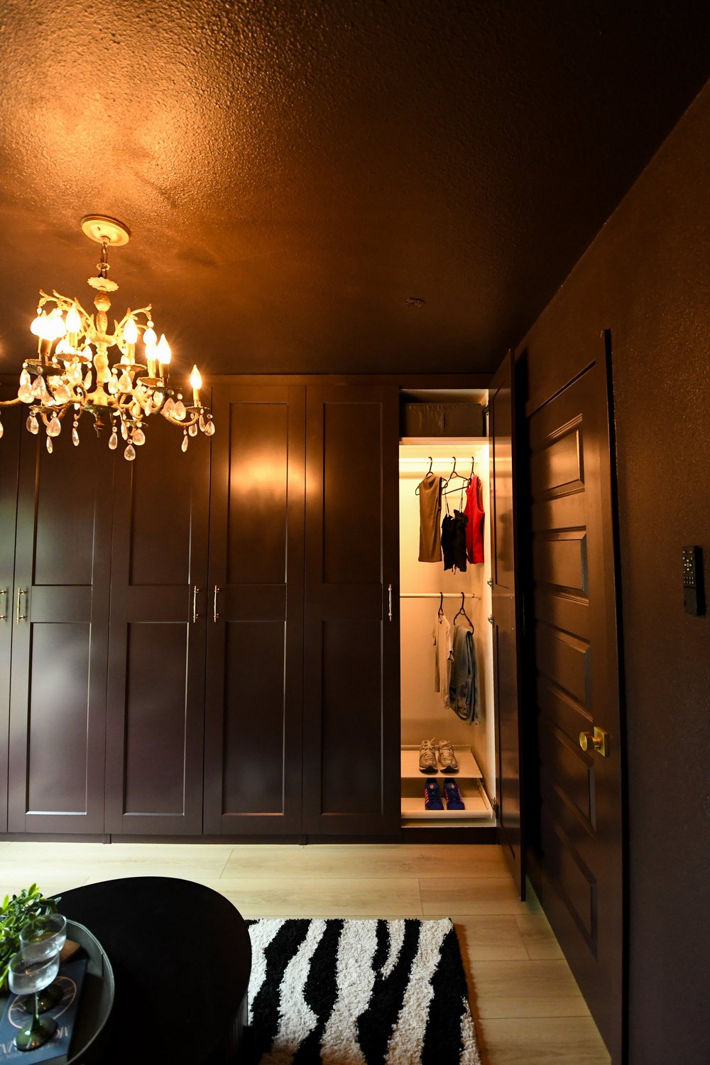 Chocolate brown built-in wardrobes down the length of the room with the lit closet beyond