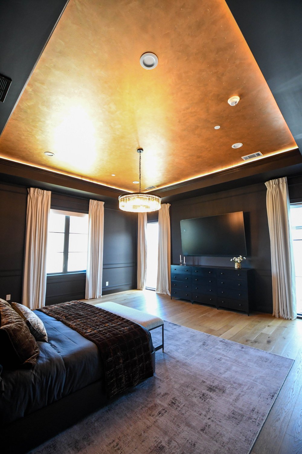 The room from the corner with the gold ceiling, dark dresser and a TV on the far wall