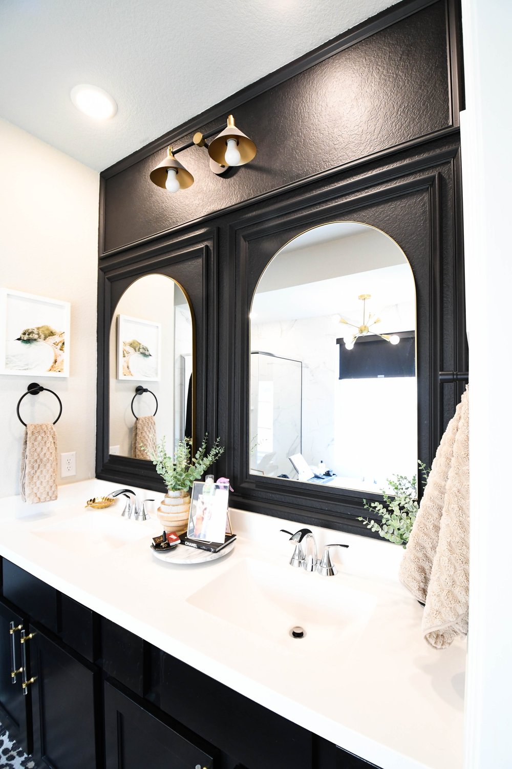 Double vanity under a black framed millwork surround with two arched mirrors