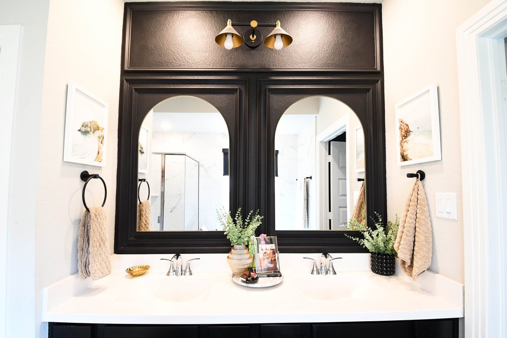 Black millwork surround with two arched mirrors and brass sconces above the vanity