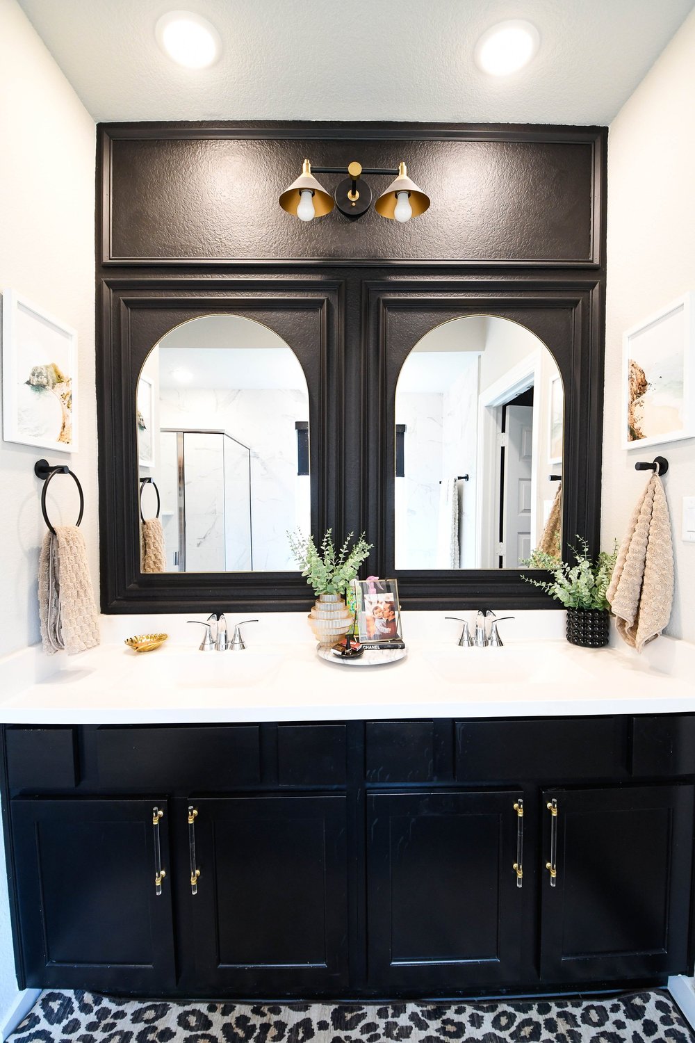 The black double vanity straight on with arched mirrors and a leopard print rug