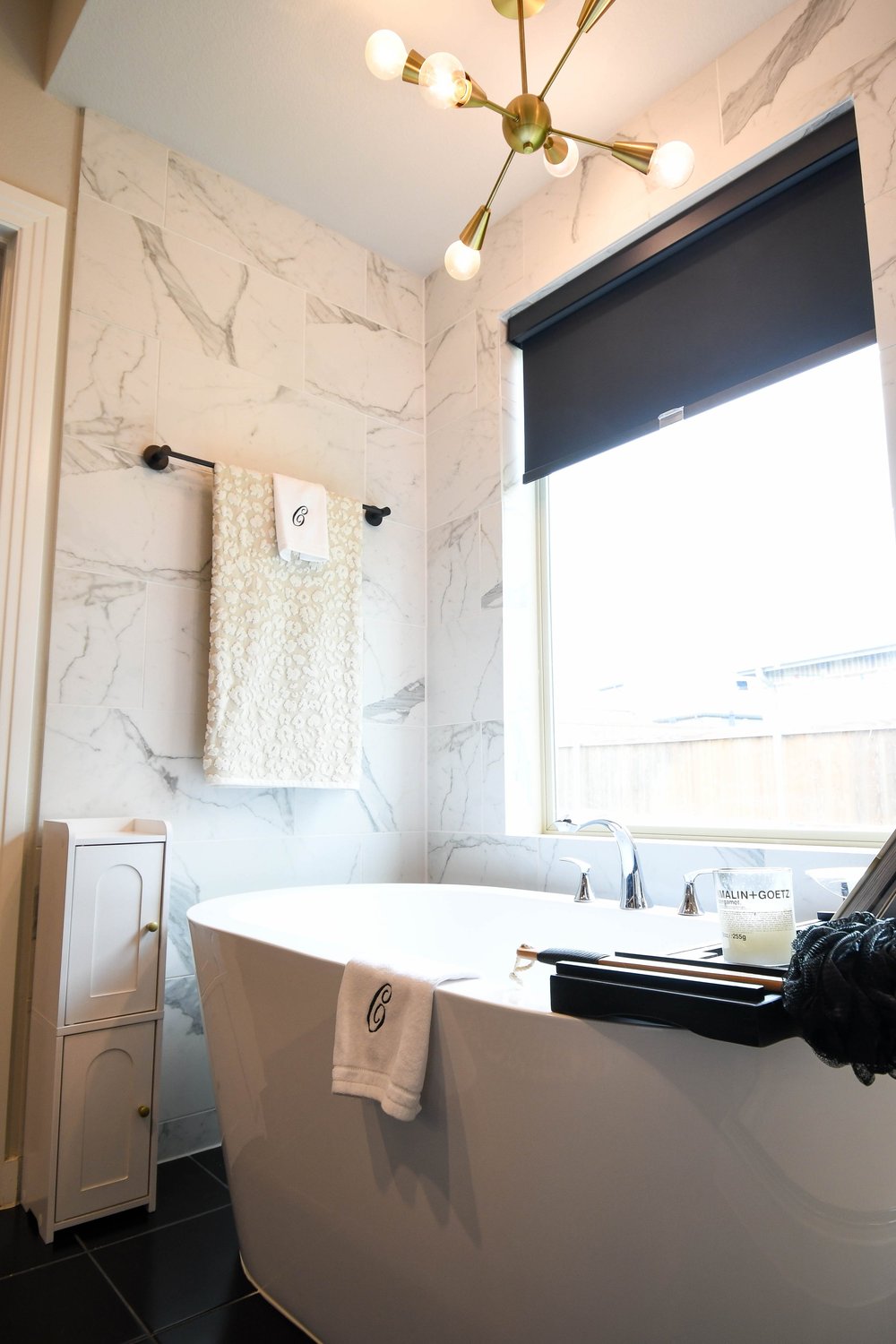 Freestanding tub below the window with a linen tower alongside