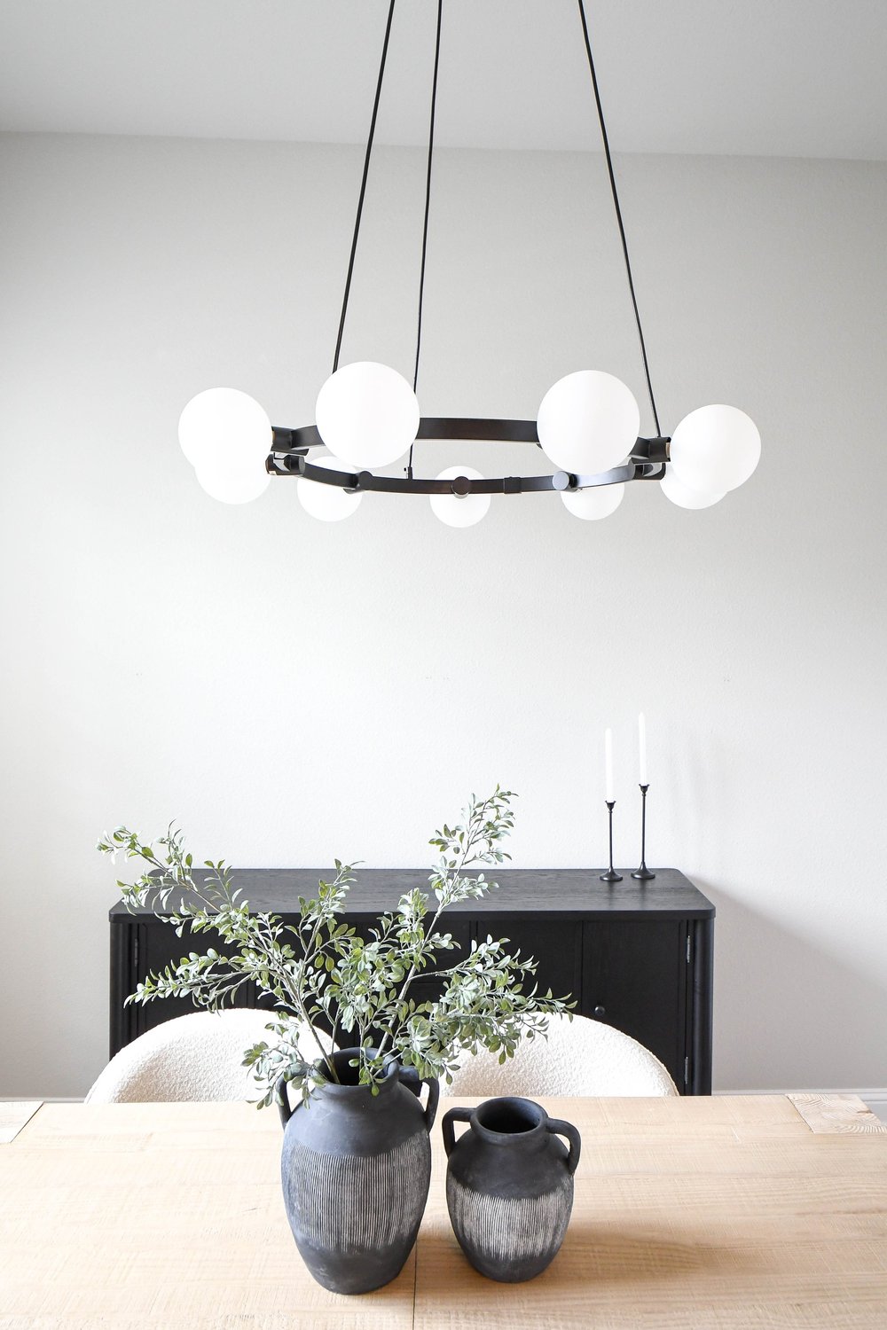 Black pottery and olive branches on the dining table under the globe ring chandelier