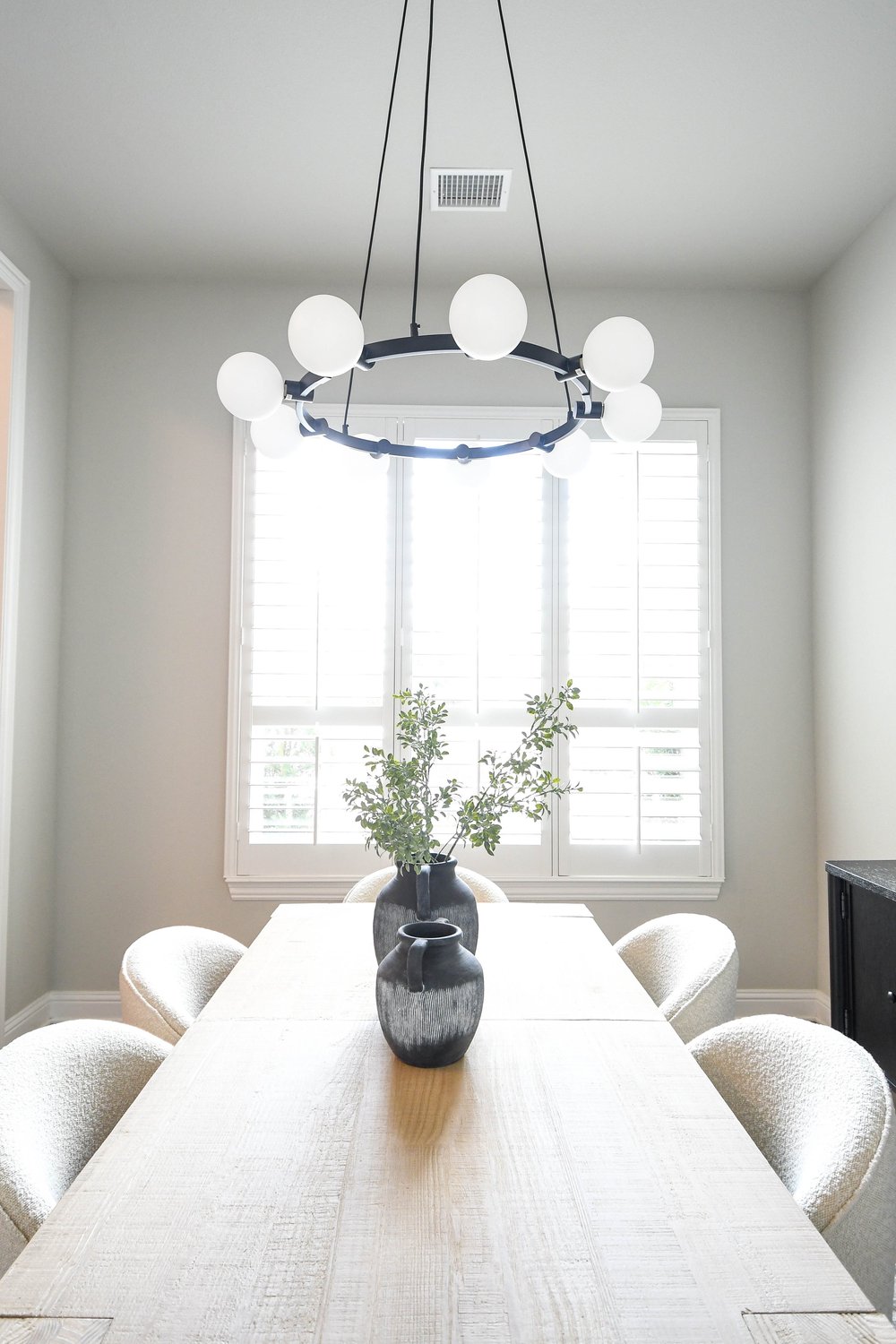 Long white oak dining table with boucle chairs in front of a shuttered window