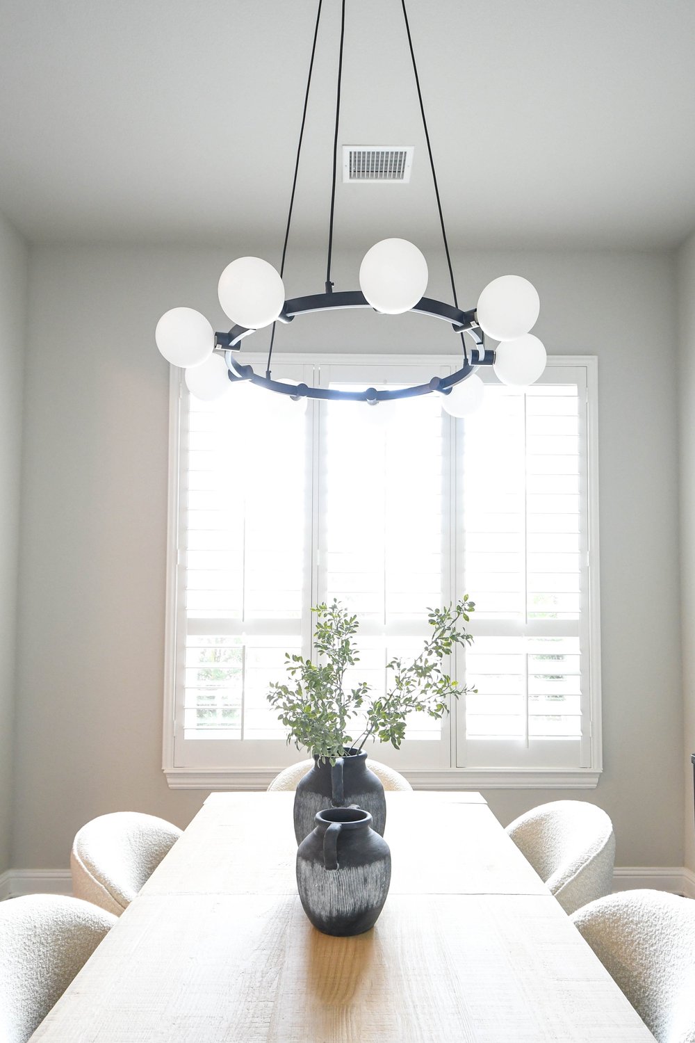 The dining table and boucle chairs lit by the window with the globe chandelier above