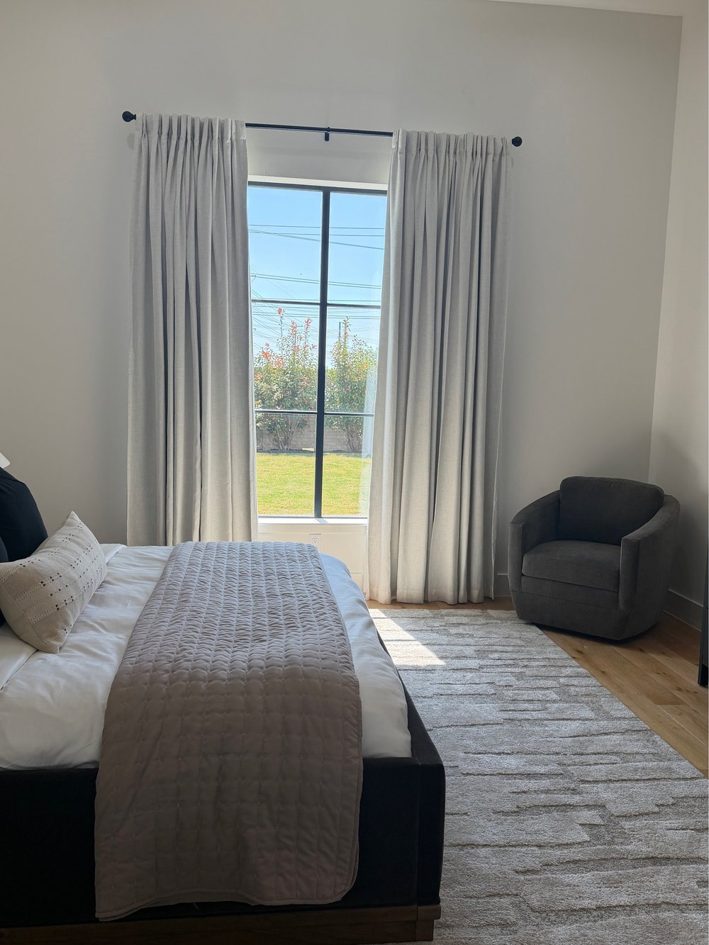Bedroom with a dark upholstered bed, quilted throw and a swivel chair by the window