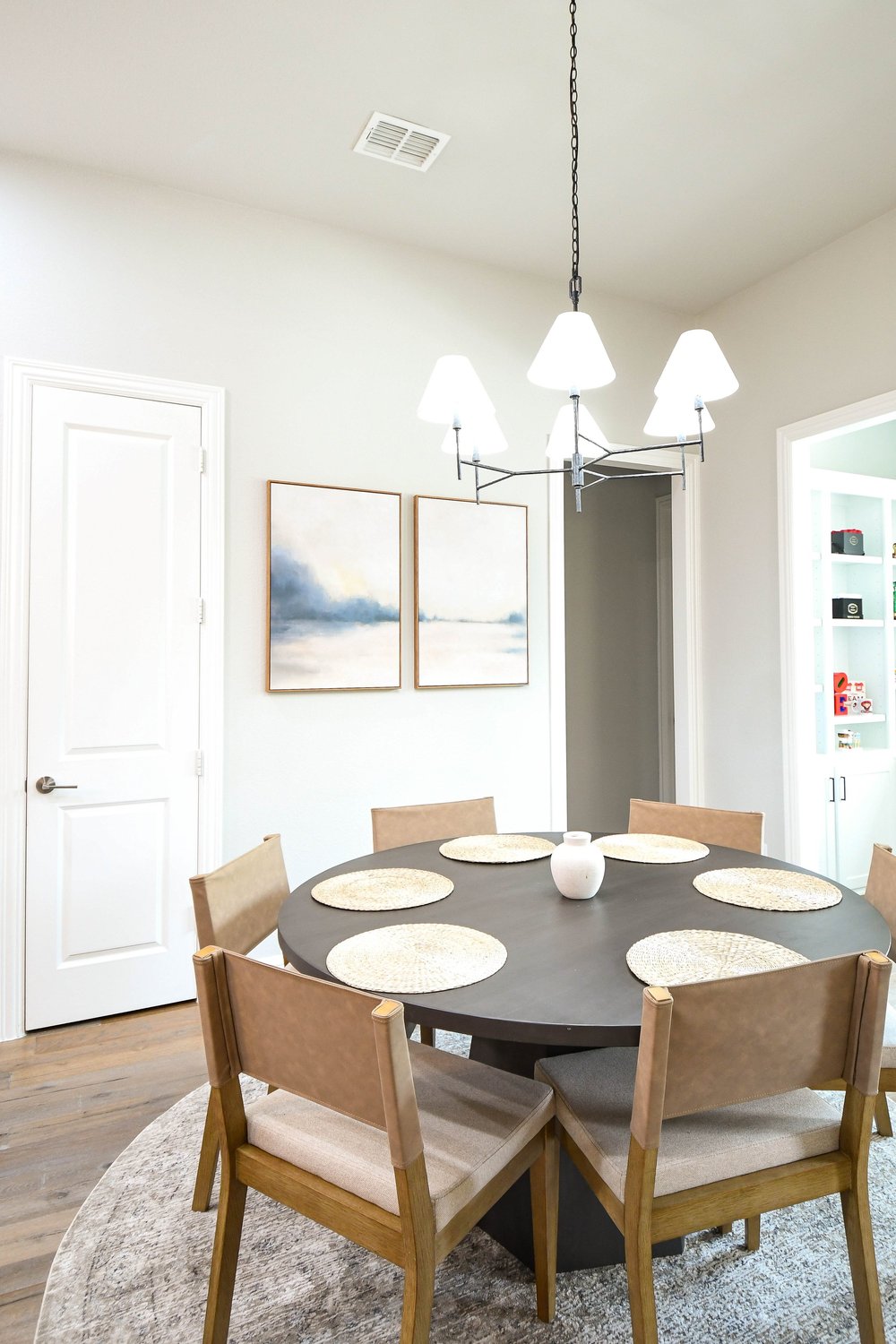 Round dining table with wood chairs beneath a white shaded chandelier