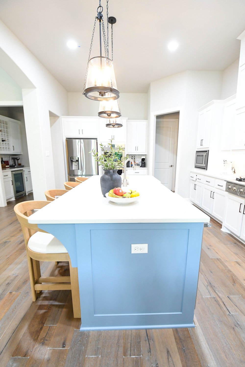 Blue grey island with oak stools running toward the refrigerator wall