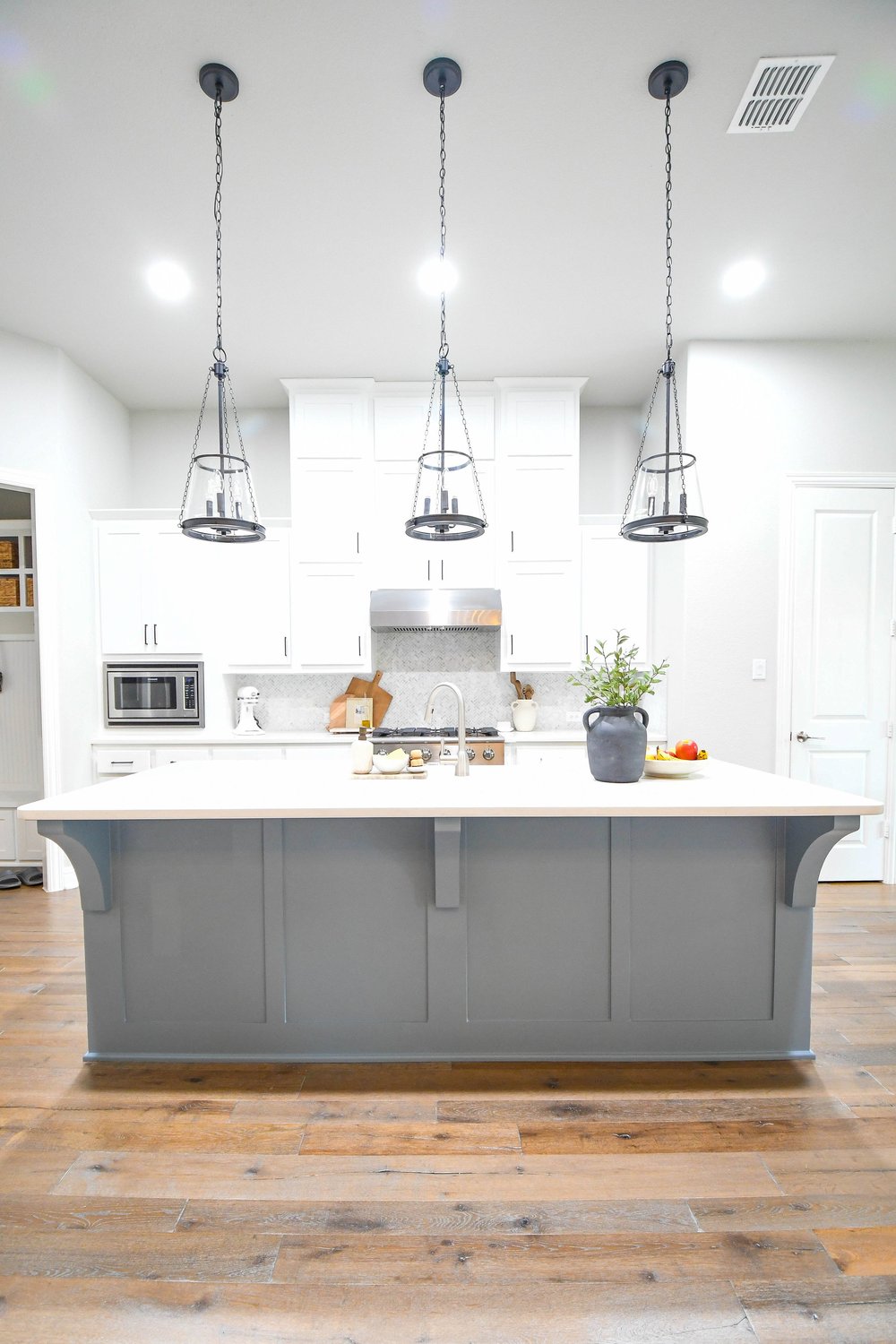 Kitchen island straight on with three lantern pendants and the range hood