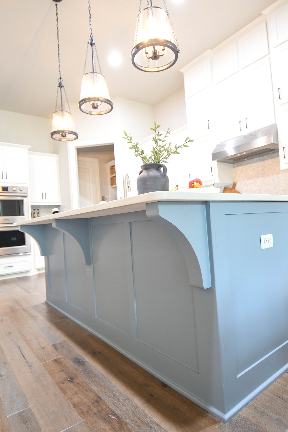 The island from the far end with the wall ovens and pendant lights