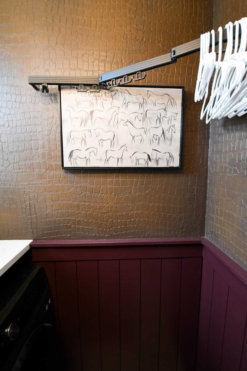 Framed line drawing of horses above the burgundy panelling with hangers on the rail