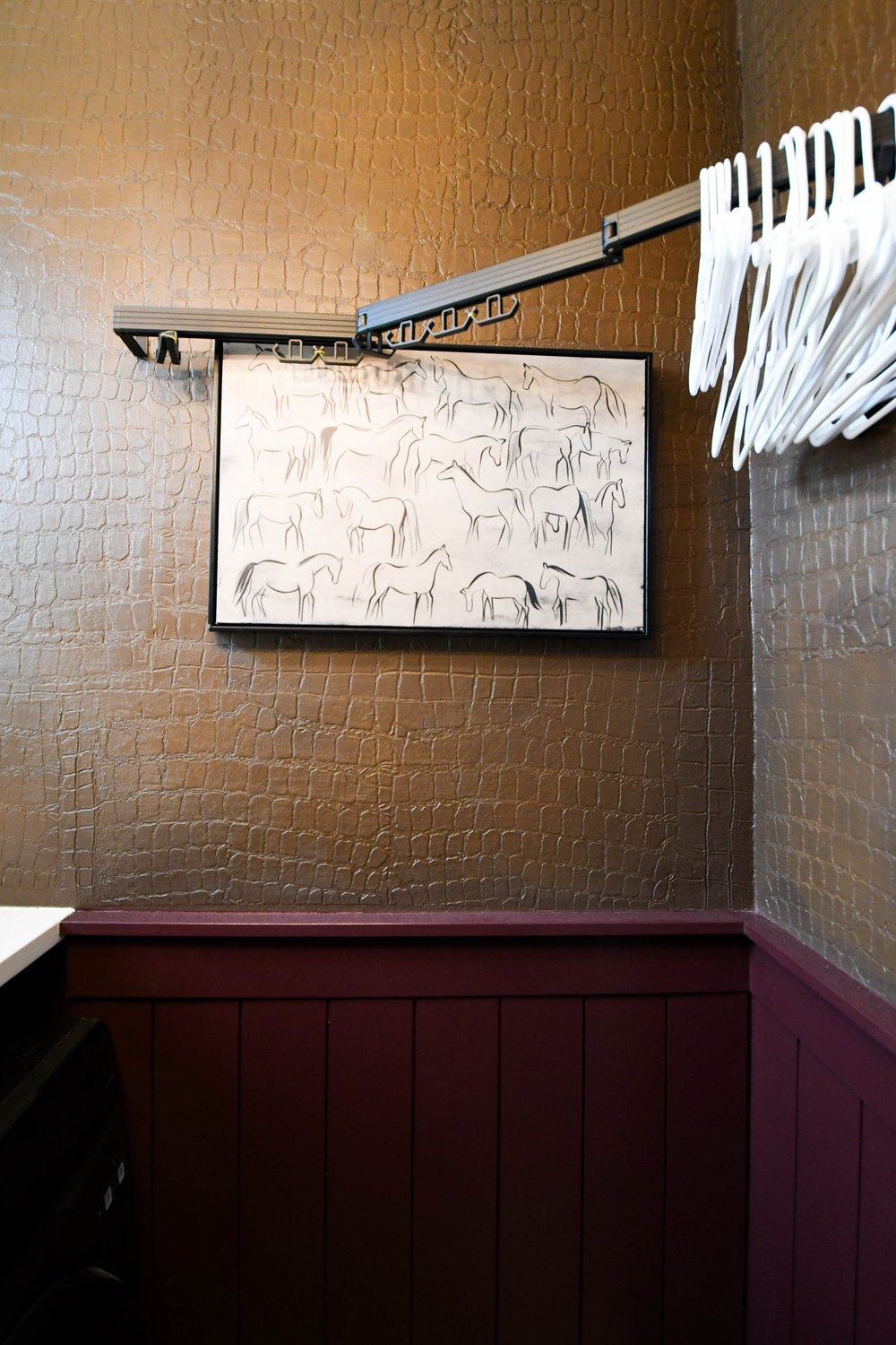 The horse artwork and hanging rail on the textured wall