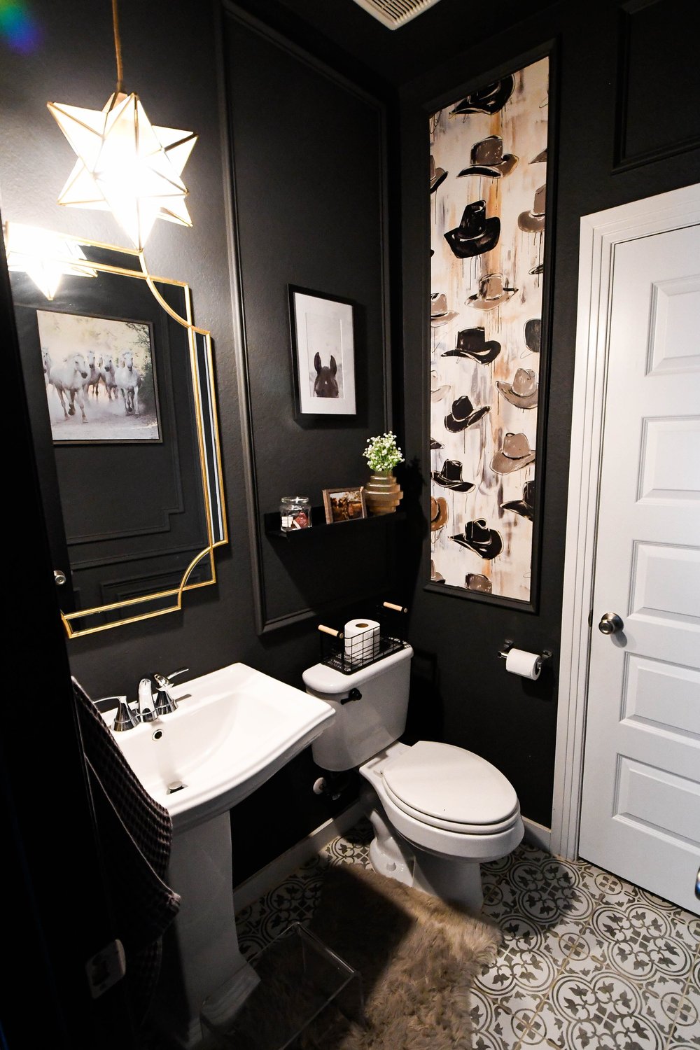 Powder bath with a black wall, pedestal sink and a cowboy hat wallpaper panel