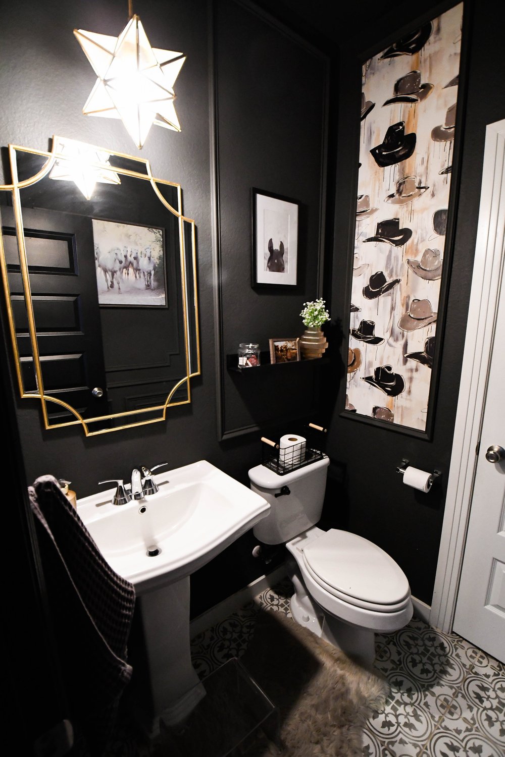 Pedestal sink and gold mirror below a star pendant in the black powder bath