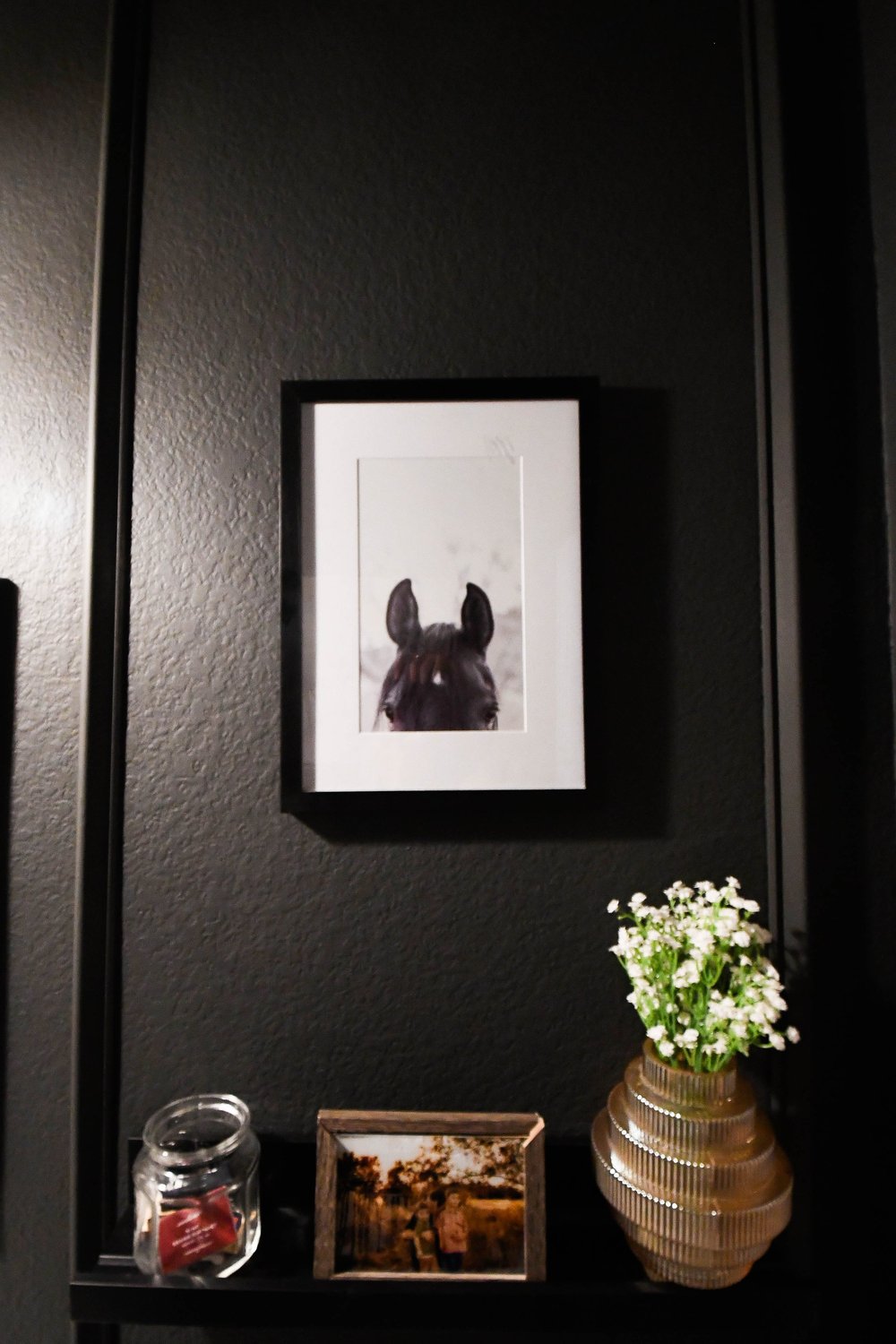 Framed dog portrait above a black shelf with a brass vase of flowers