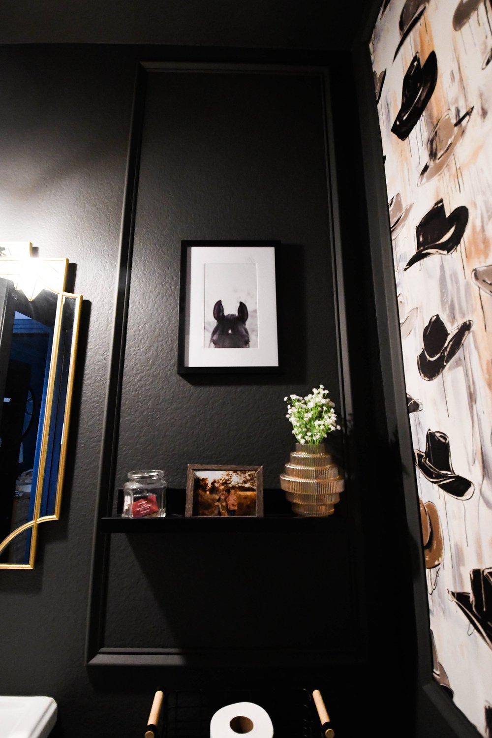 The shelf, framed art and hat wallpaper beside the gold mirror