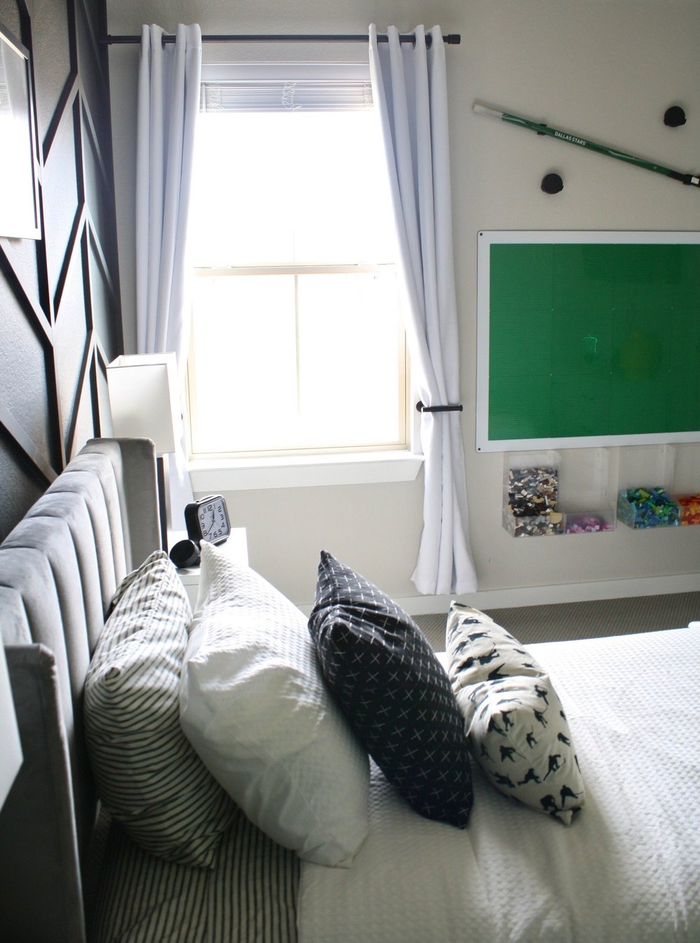 Twin bed against a black herringbone panel wall with a hockey stick above the window