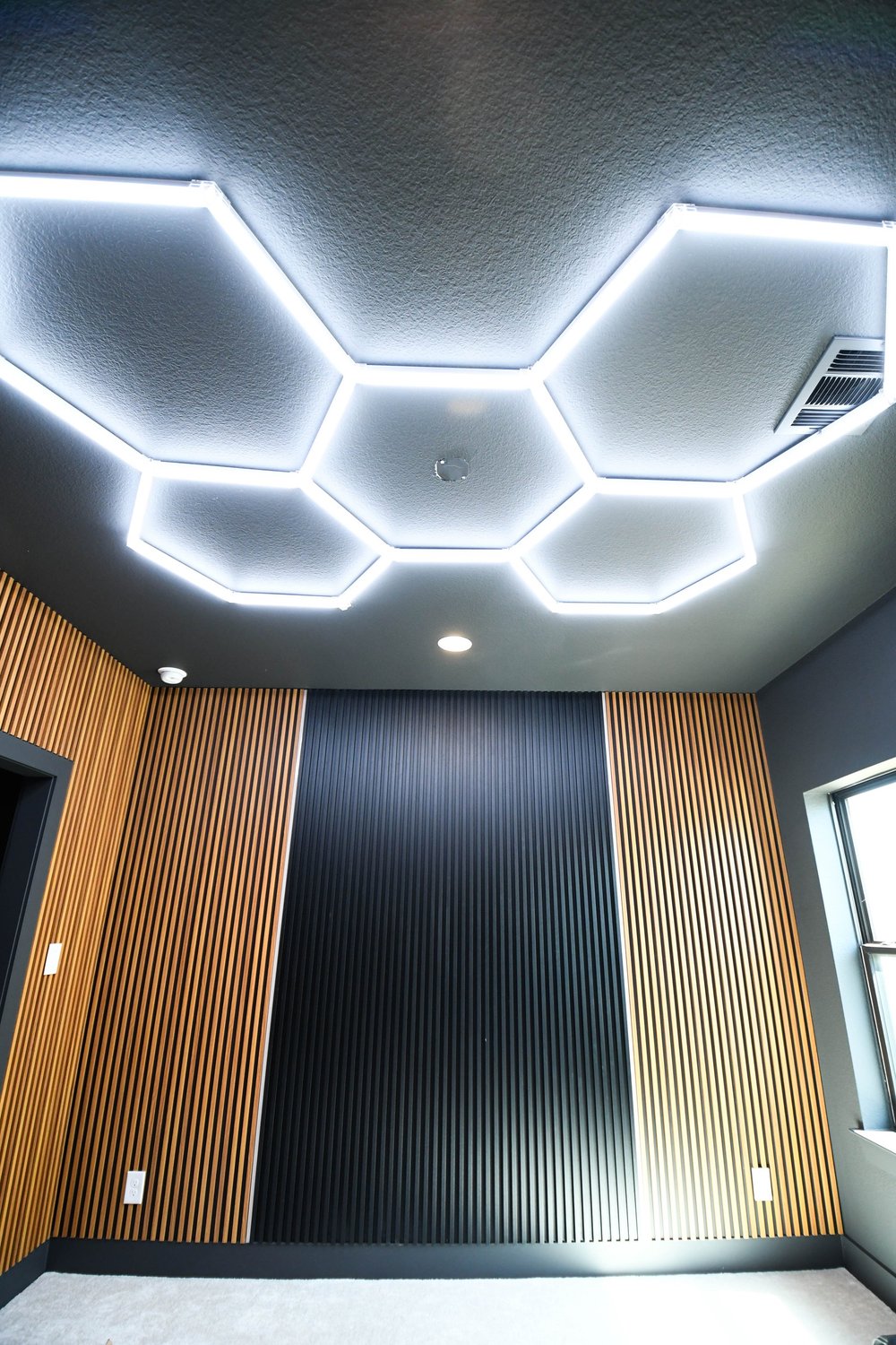 Hexagon LED ceiling lights above a charcoal fluted wall and wood slat panels