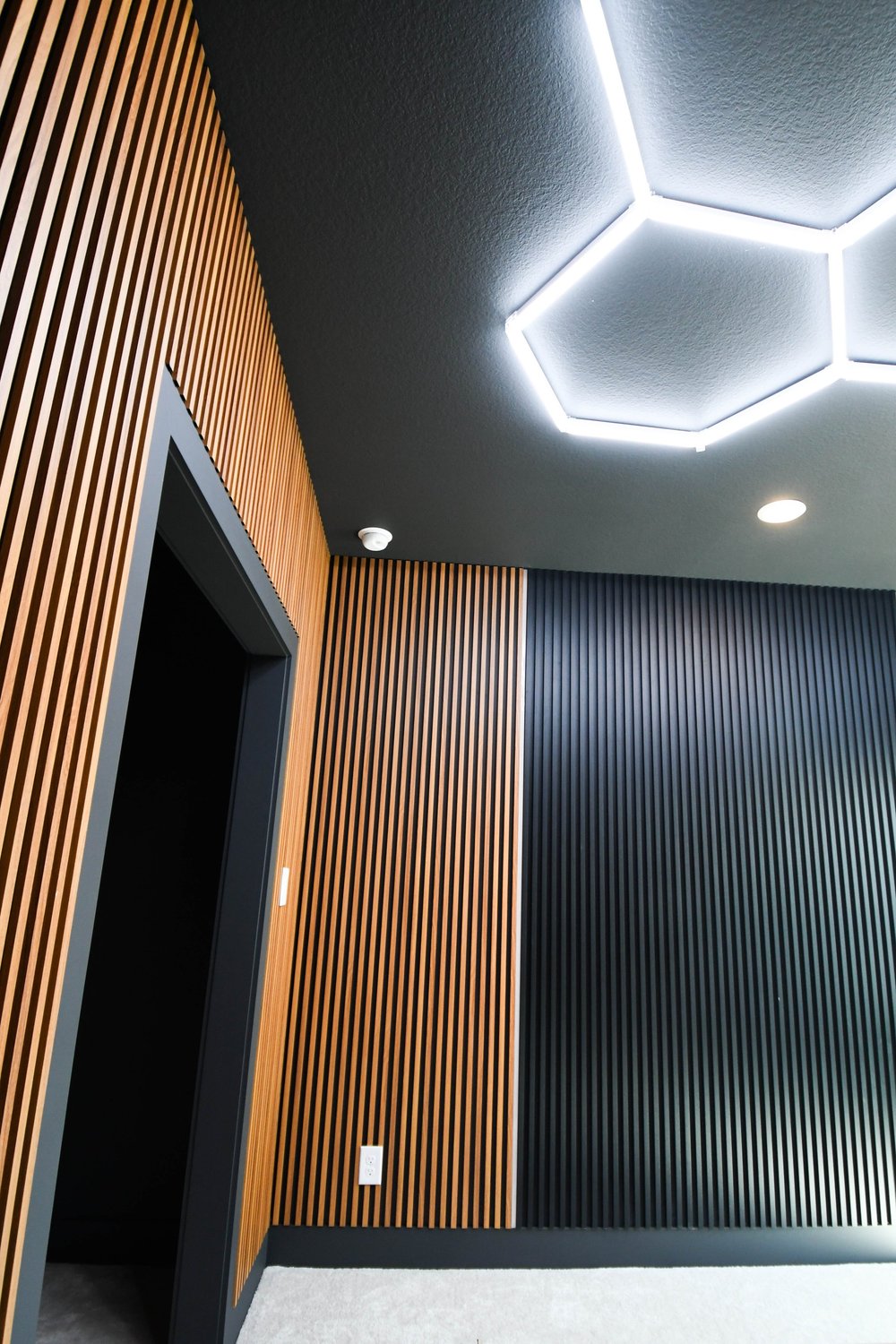 The slat and fluted panels meeting at the door under the hexagon lighting
