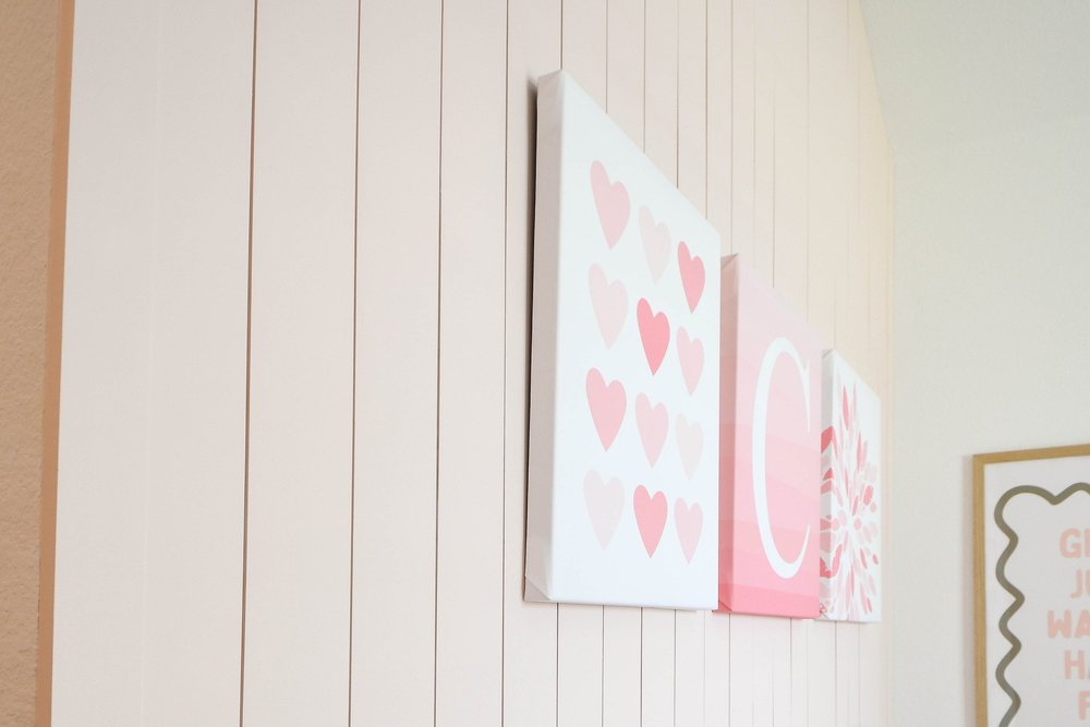 Angled view of the pink canvases against the vertical plank wall