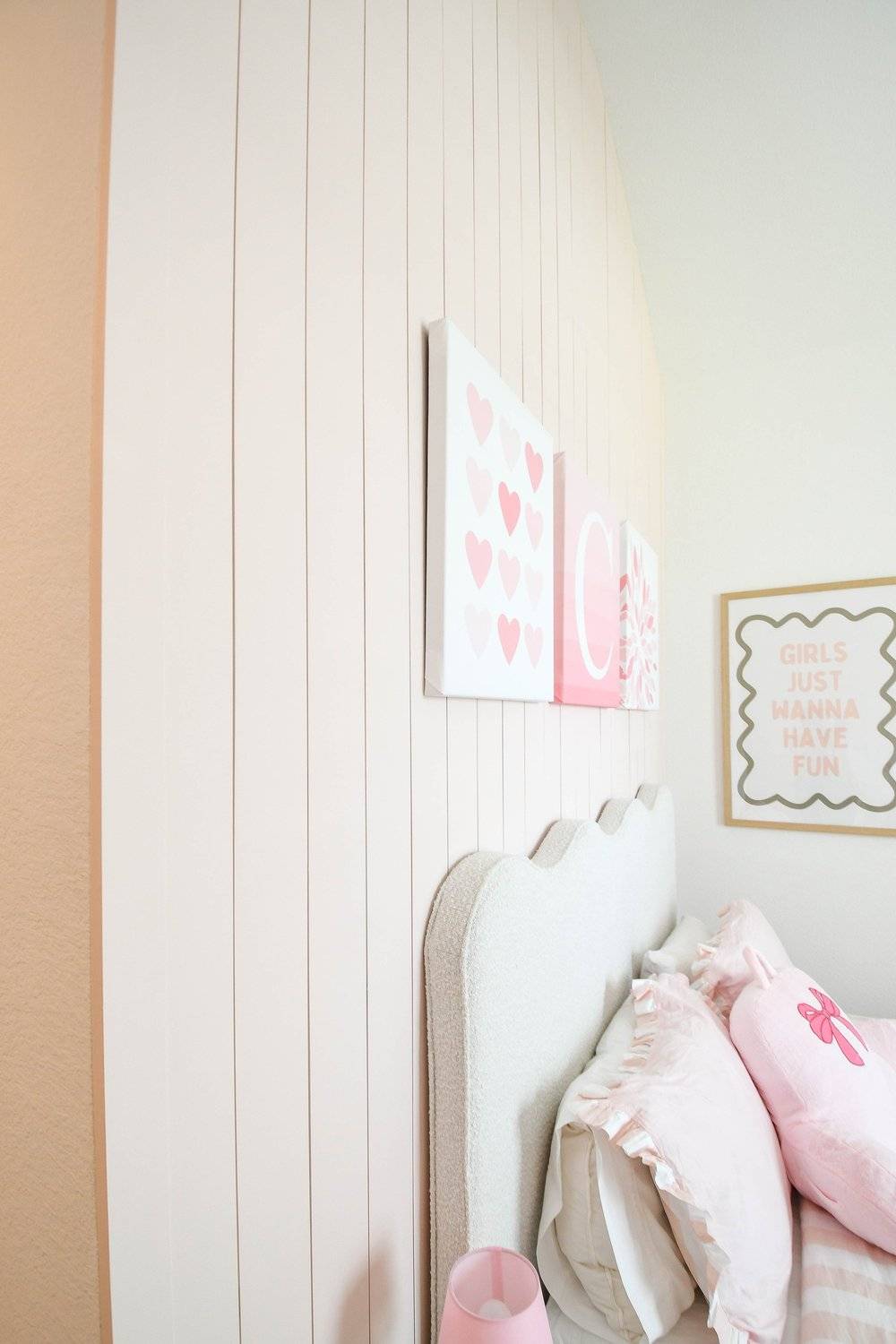 Scalloped upholstered headboard and ruffled pink pillows against the planked wall