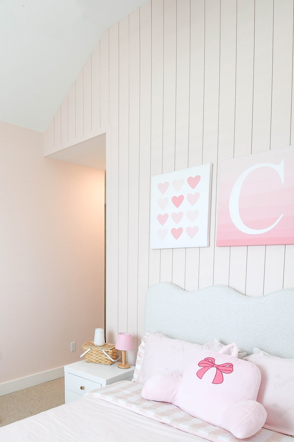 The nightstand and the bed's pink bow pillow against the plank wall
