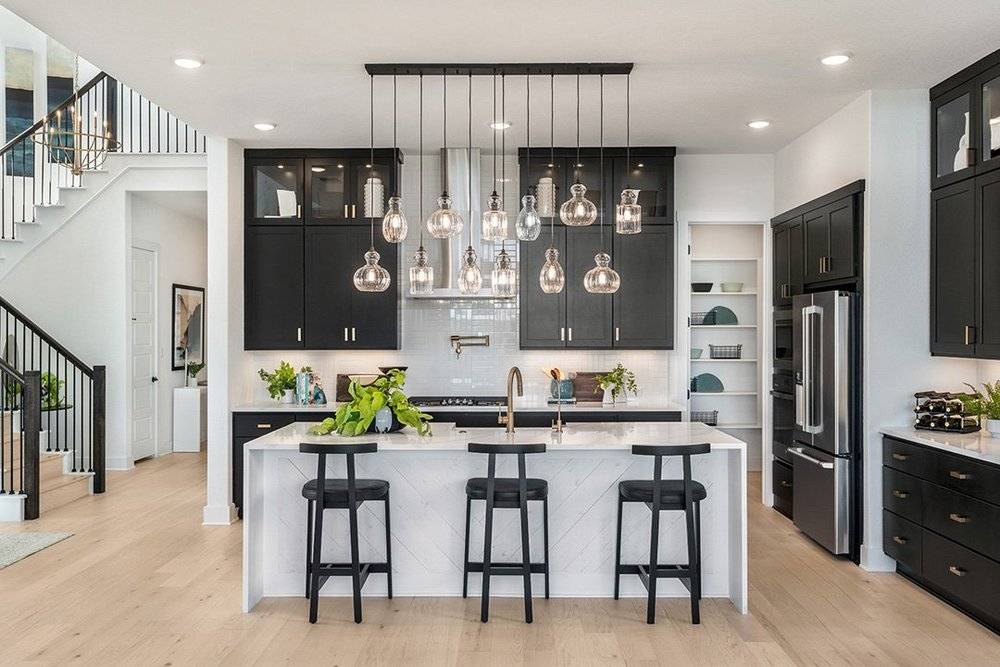 Kitchen with black cabinetry, a white waterfall island and glass pendant lights
