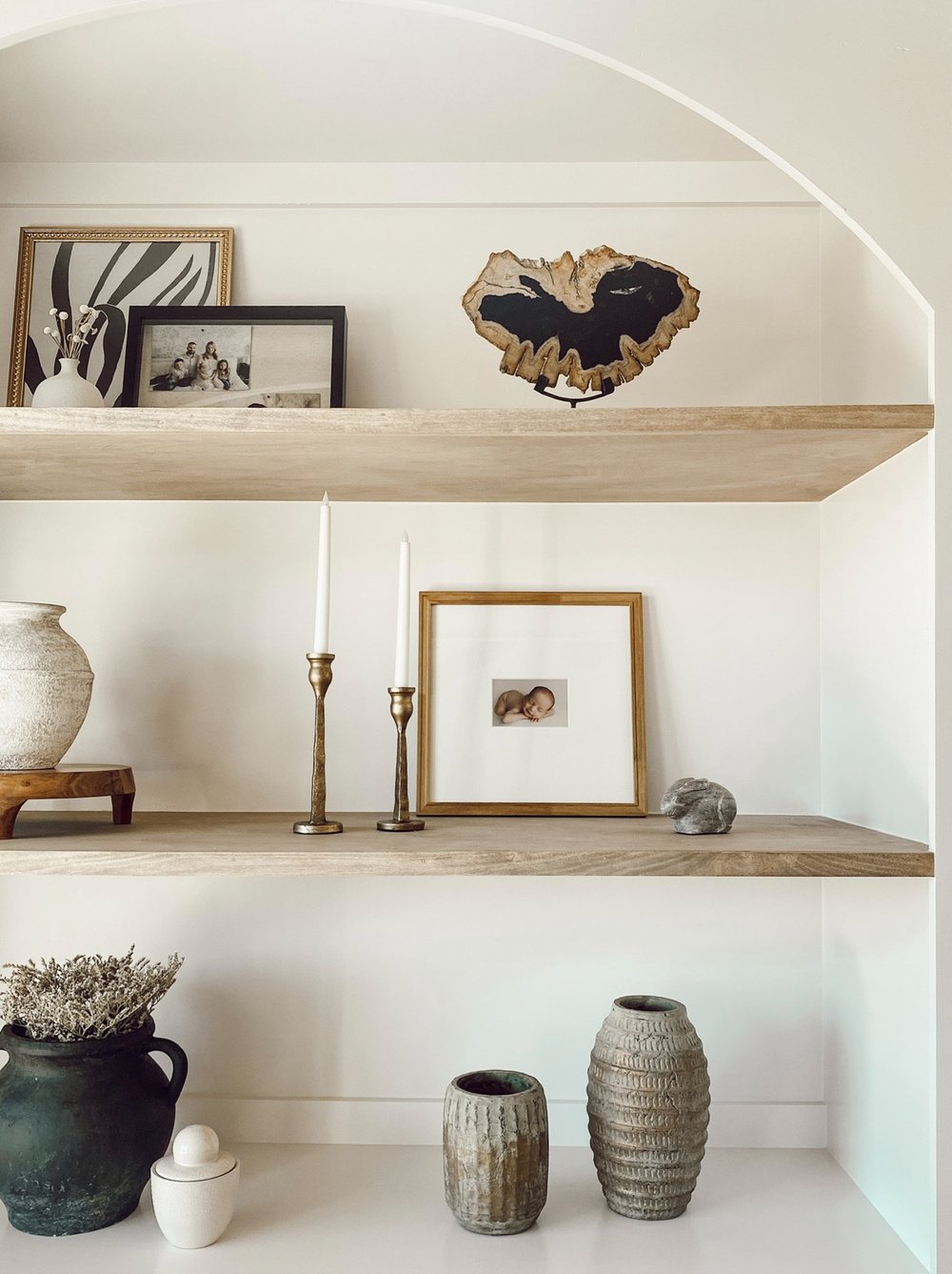 Arched niche with floating oak shelves styled with pottery, candlesticks and framed art