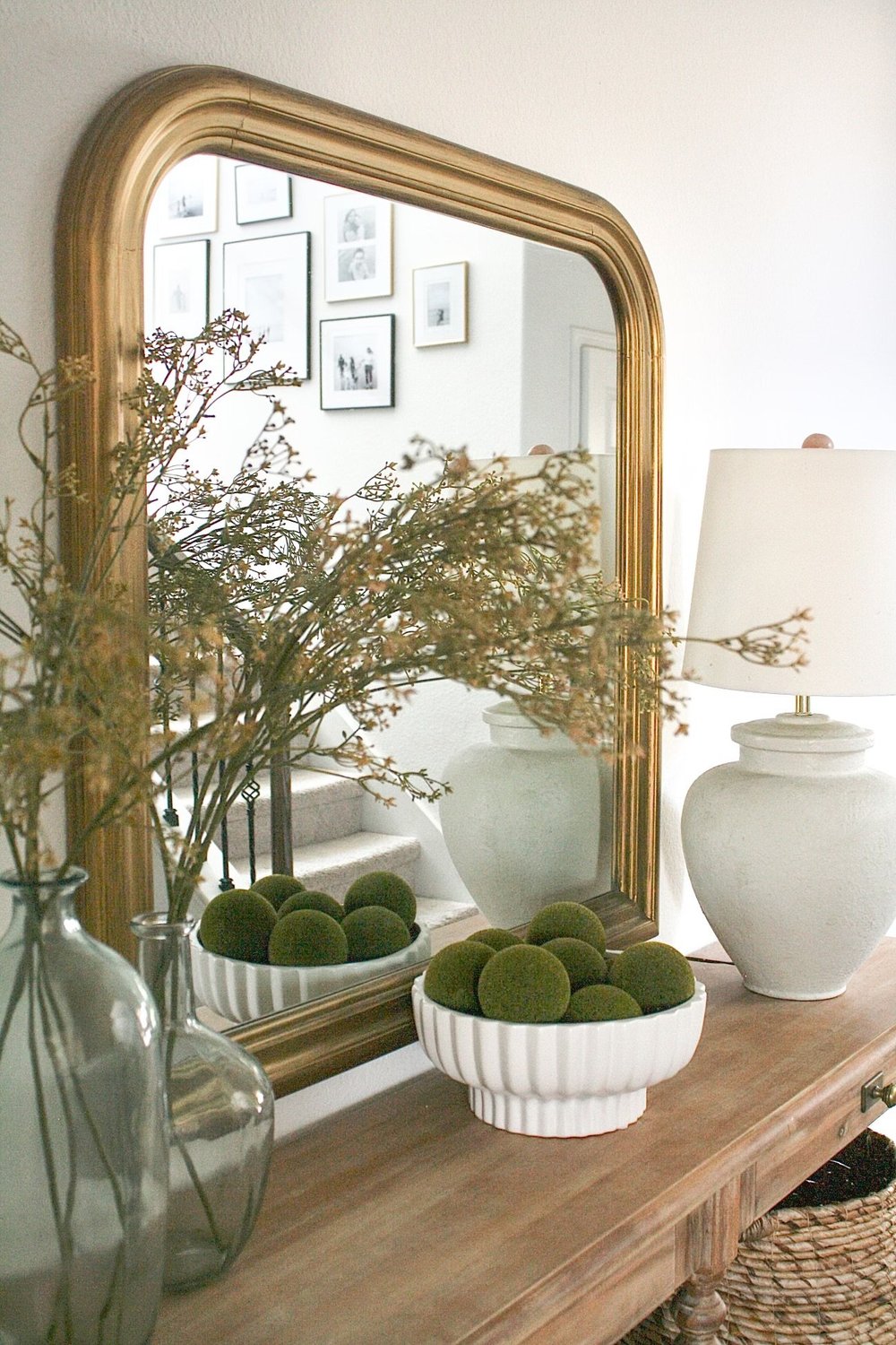 Entry console with a large arched gold mirror, a stoneware lamp and moss in a fluted bowl