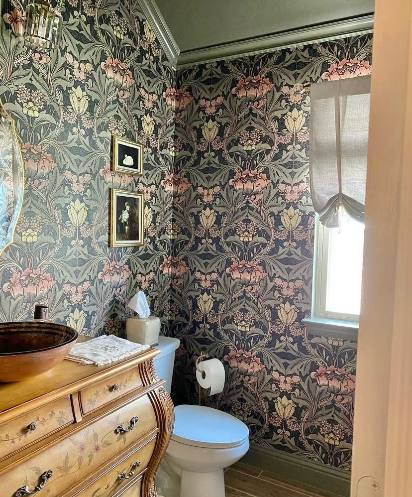 Powder room in dark floral wallpaper with a hammered copper vessel sink on a wood chest