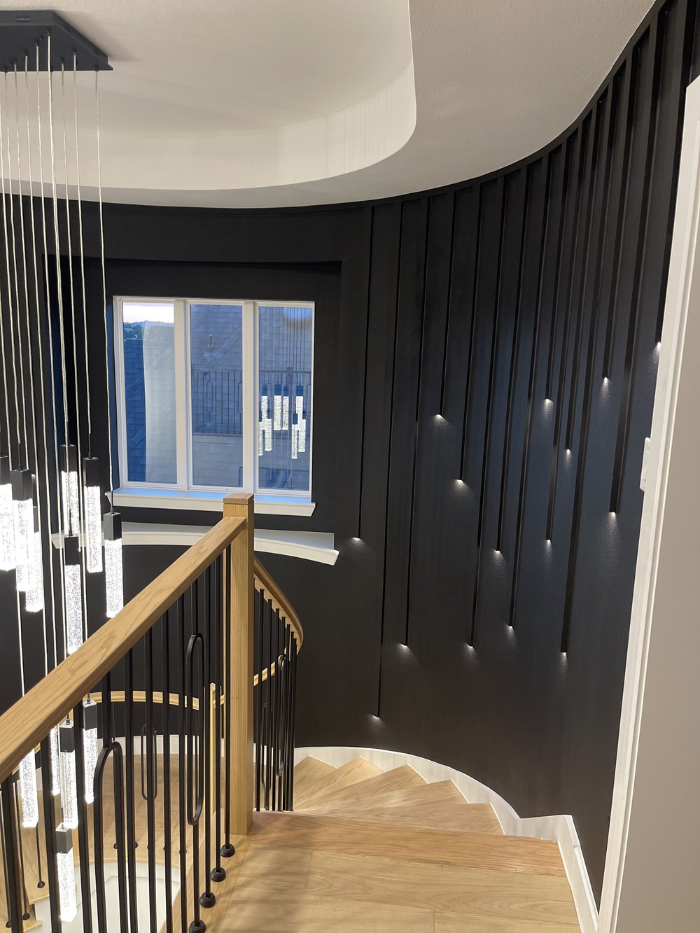 Looking down the curved stair at the black vertical slat wall with recessed step lights