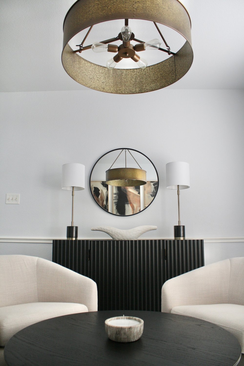 Fluted credenza under a round mirror flanked by two column lamps