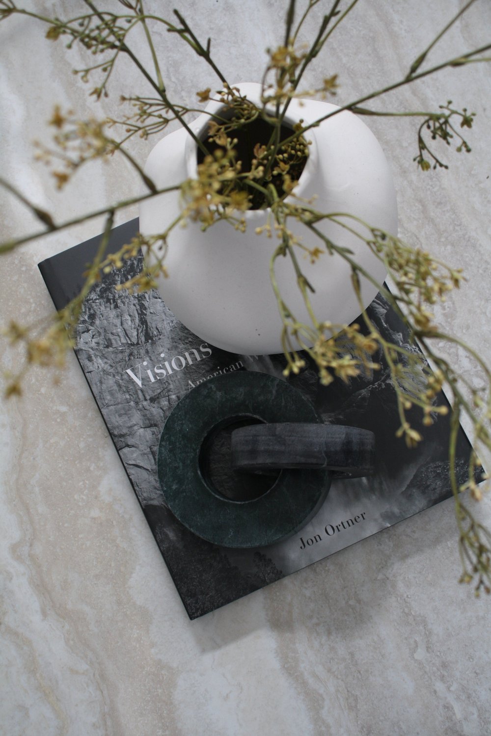 White vase and branches on a stack of art books on a travertine table