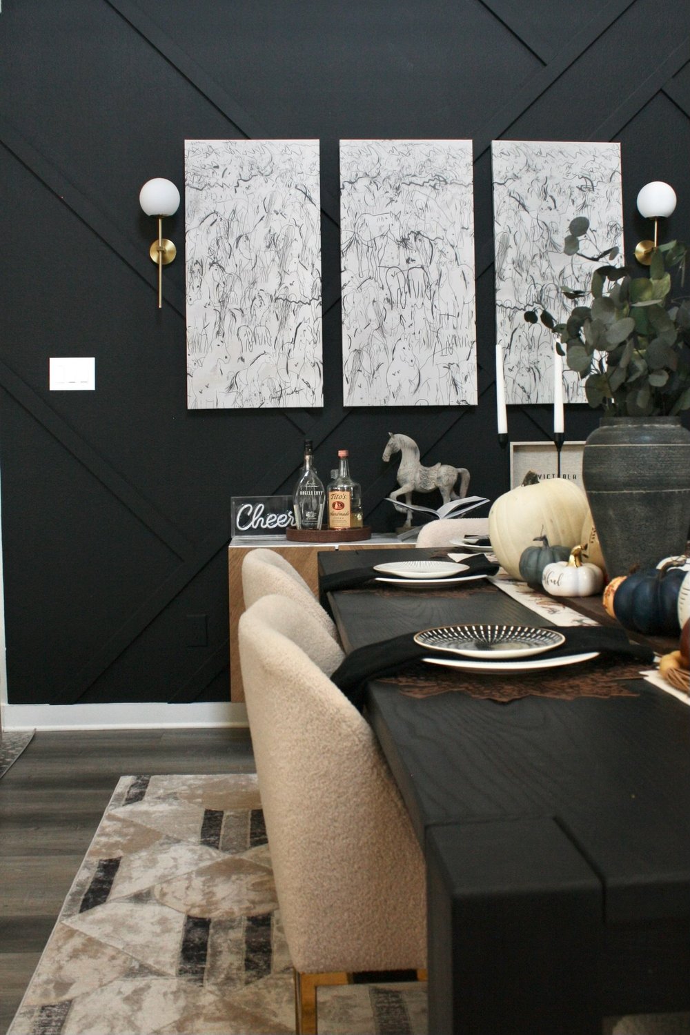 Dining table set against a black board and batten wall hung with three abstract canvases