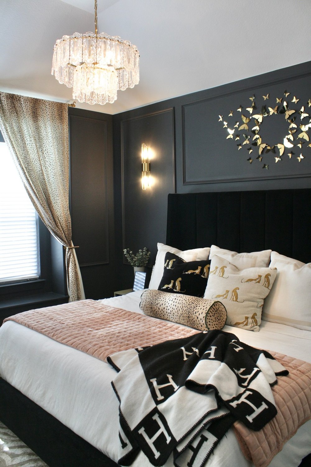 Bedroom with a black velvet headboard, crystal chandelier and gold butterfly wall art