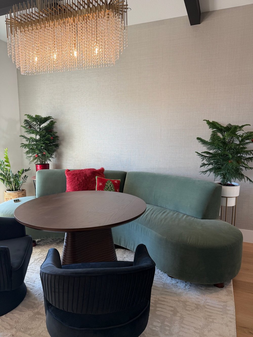 Sage curved sofa and black barrel chairs around a walnut table under a beaded chandelier