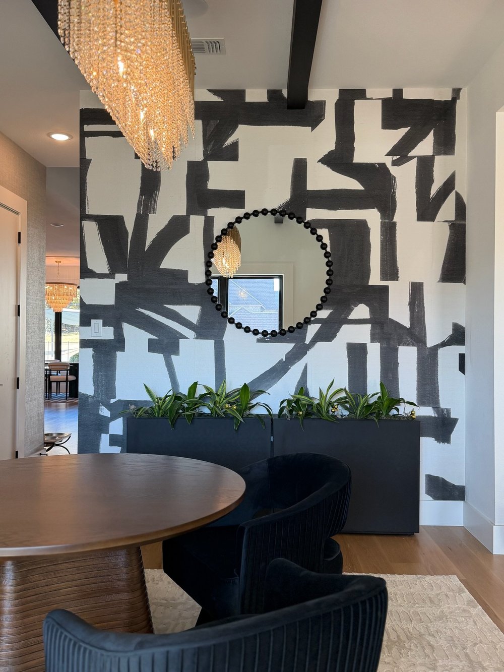 Black and white abstract mural wall with a gold sunburst mirror above a planter box