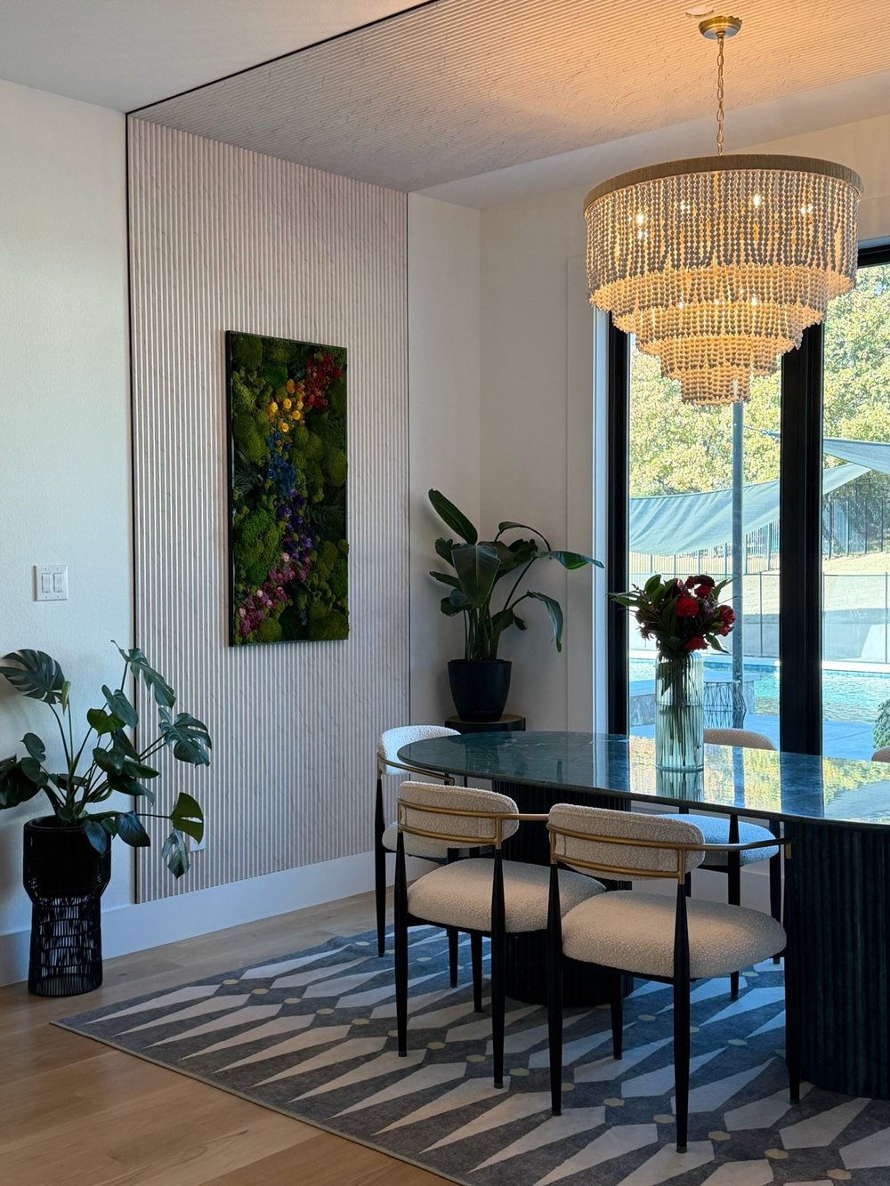 Dining area with a green stone table, cane chairs and a beaded chandelier by the pool doors