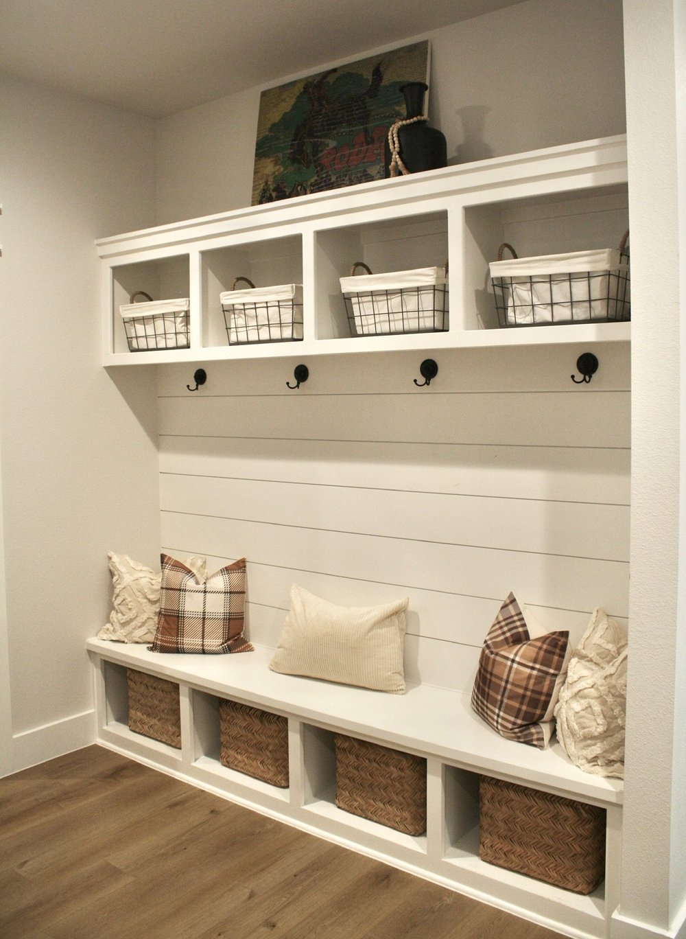 White shiplap mudroom bench with cubbies, baskets, hooks and woven storage below