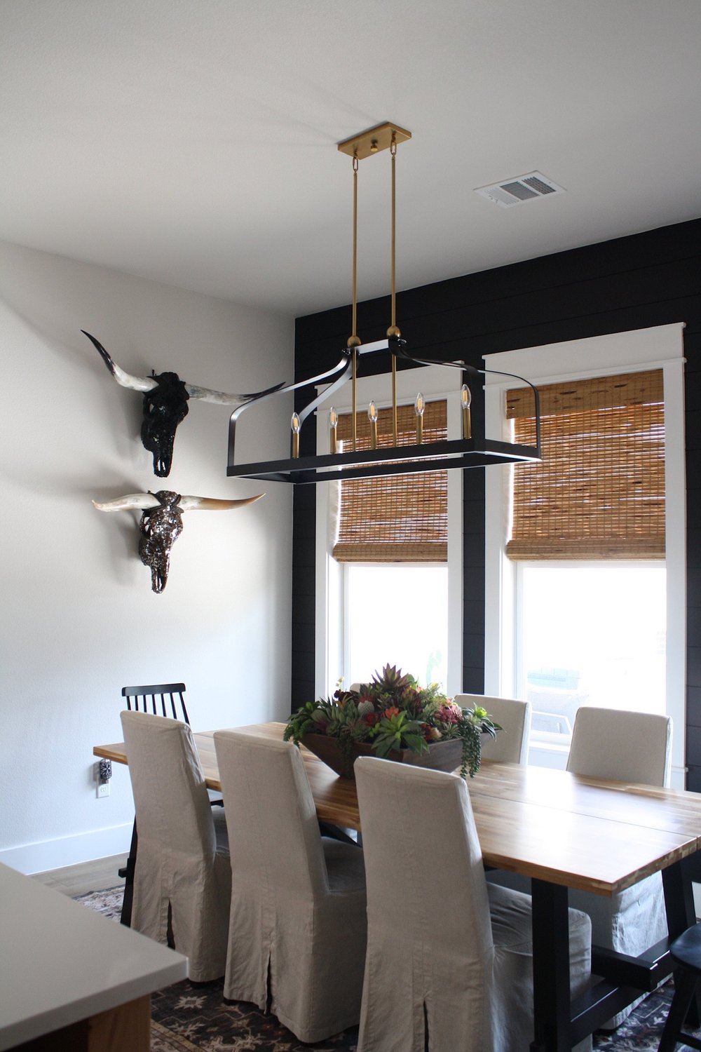 Dining table with slipcovered chairs below a linear chandelier and mounted longhorn skulls