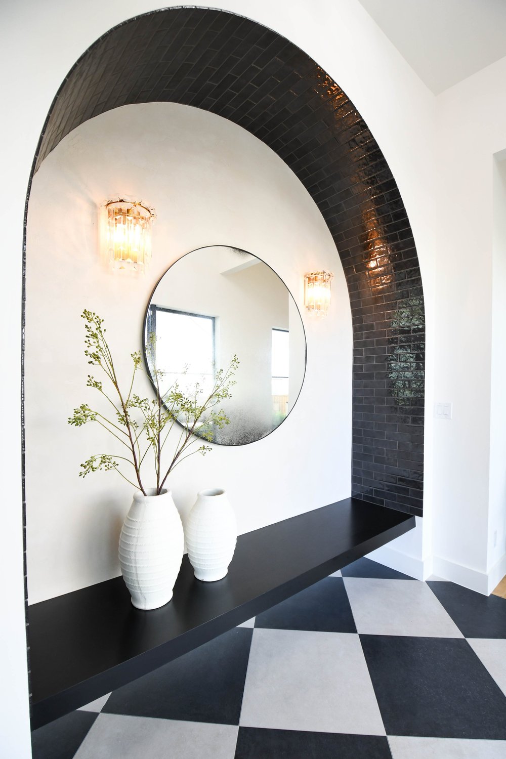 Entry with a black brick arch, round mirror and a checkerboard floor