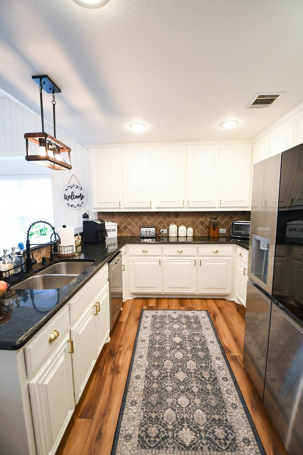 Kitchen looking down the runner past white cabinetry, black counters and stainless appliances