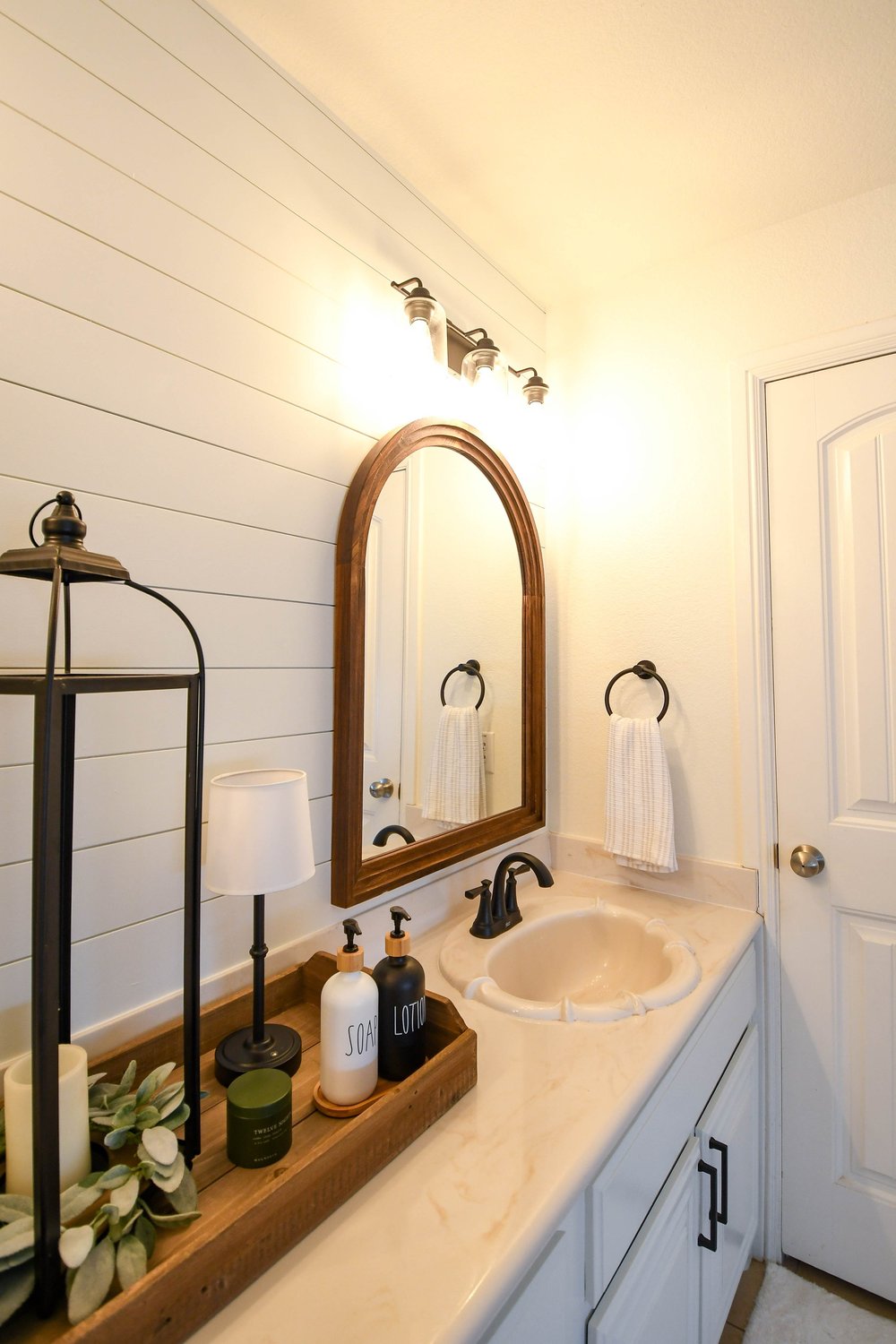 Single vanity with an arched wood mirror and a lantern on a wood tray