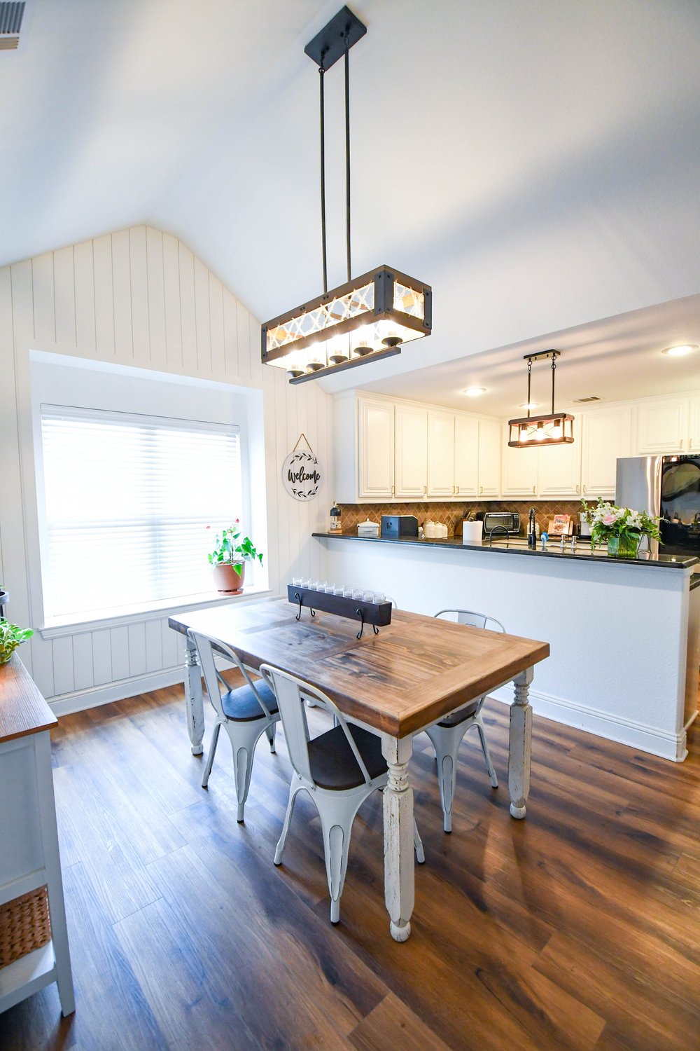 Dining table under a lantern style linear light, open to the kitchen beyond