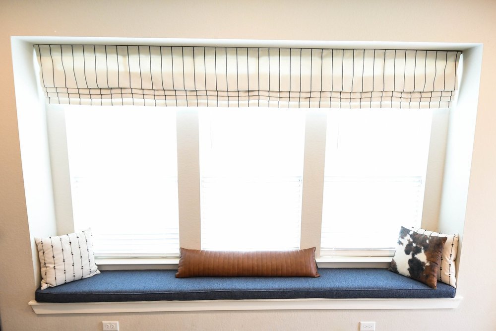 Built-in window seat with a navy cushion and leather bolster under a bay window