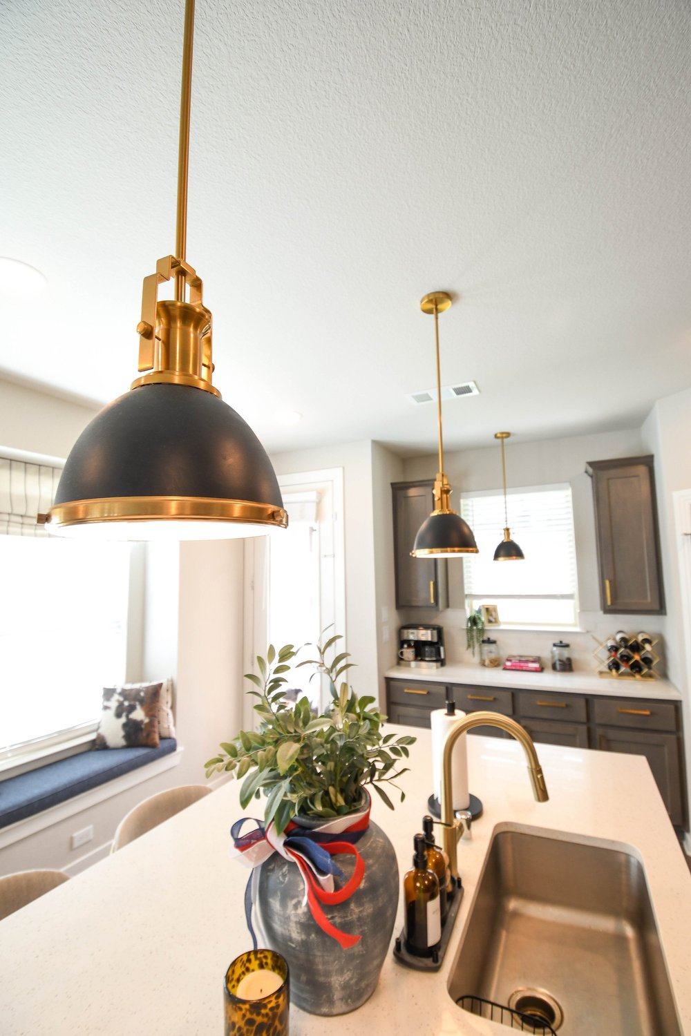 Kitchen island with a gold faucet and undermount sink below a black and brass pendant