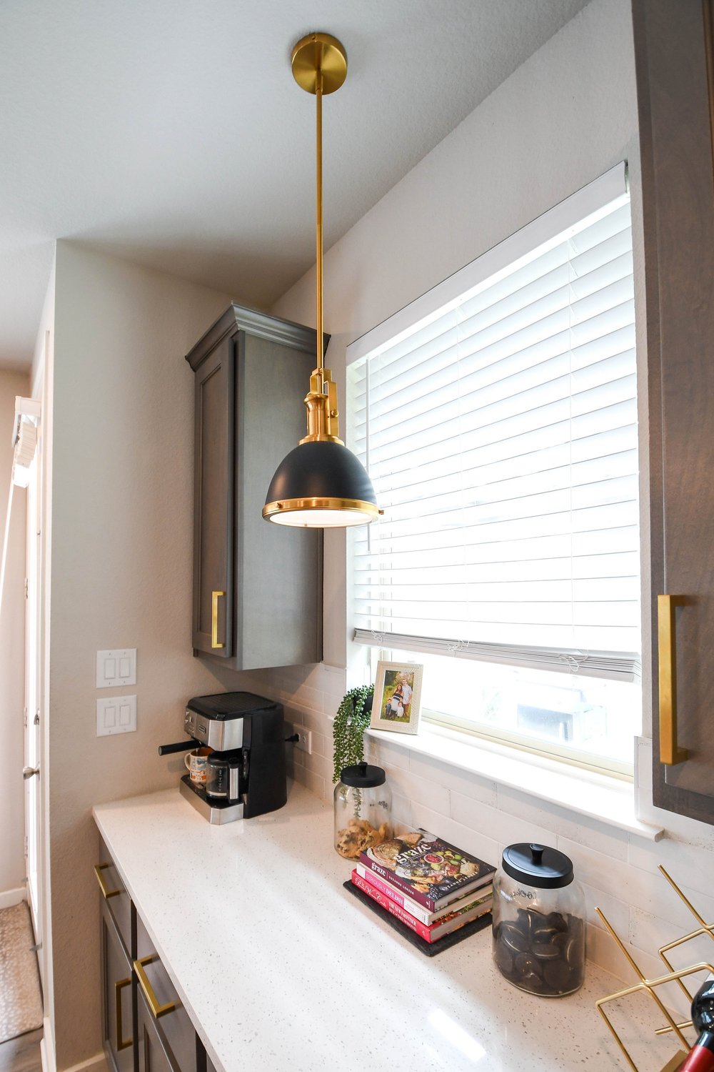 Coffee maker and brass trimmed pendant on the counter beside the window