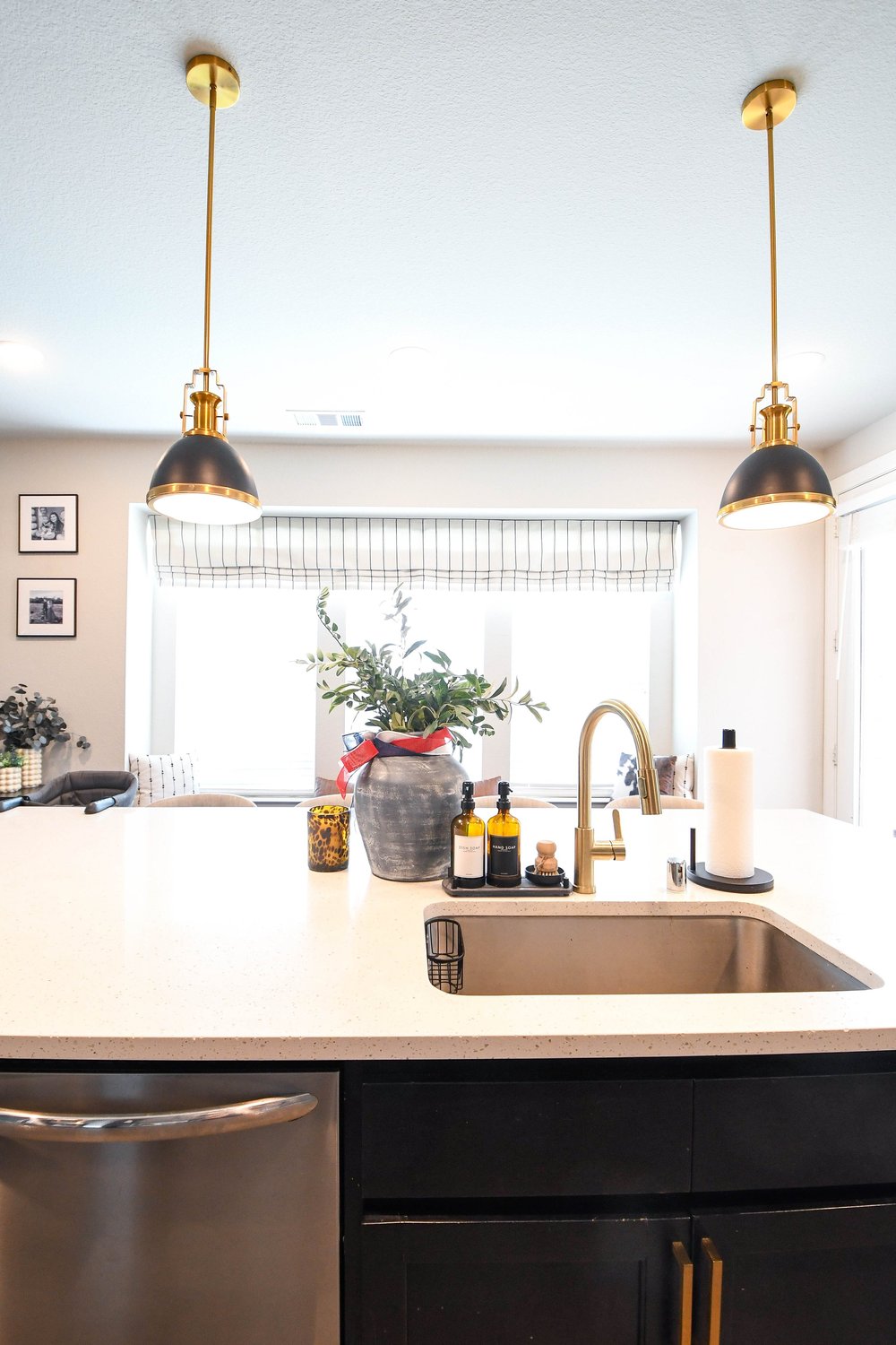 Island sink and gold faucet under two black and brass pendants